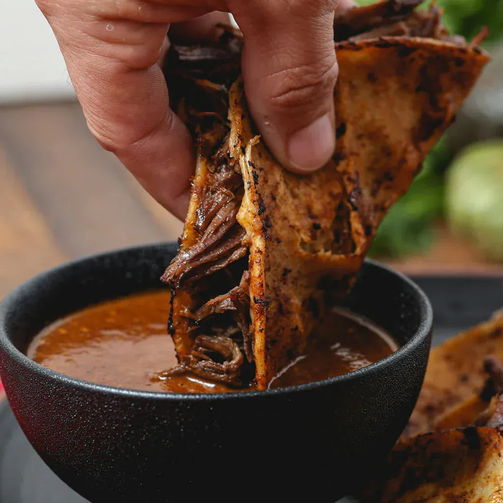 Person dipping a tortilla chip with meat into a bowl of sauce.
